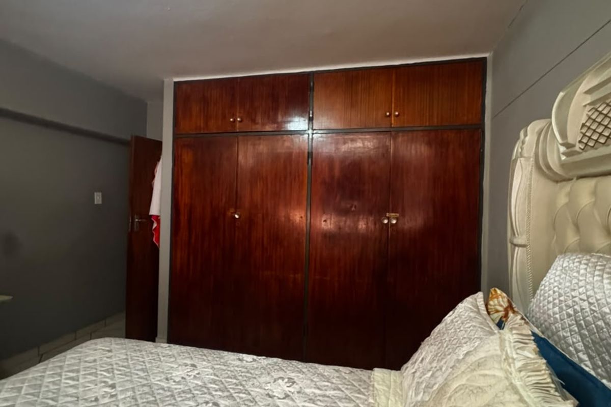 A bedroom featuring a large, floor-to-ceiling built-in wooden wardrobe with overhead storage compartments.