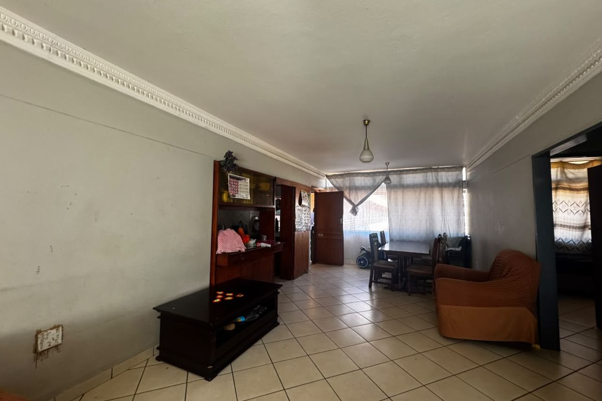 Spacious living area featuring ceramic floor tiles, decorative ceiling cornicing, and built-in cabinetry, offering a functional layout with potential for modern updates.