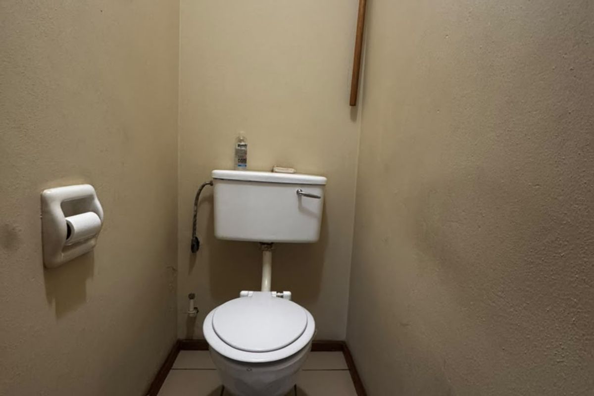 A compact, dated bathroom featuring a standard toilet, tiled flooring, and a high-level louver window for ventilation.