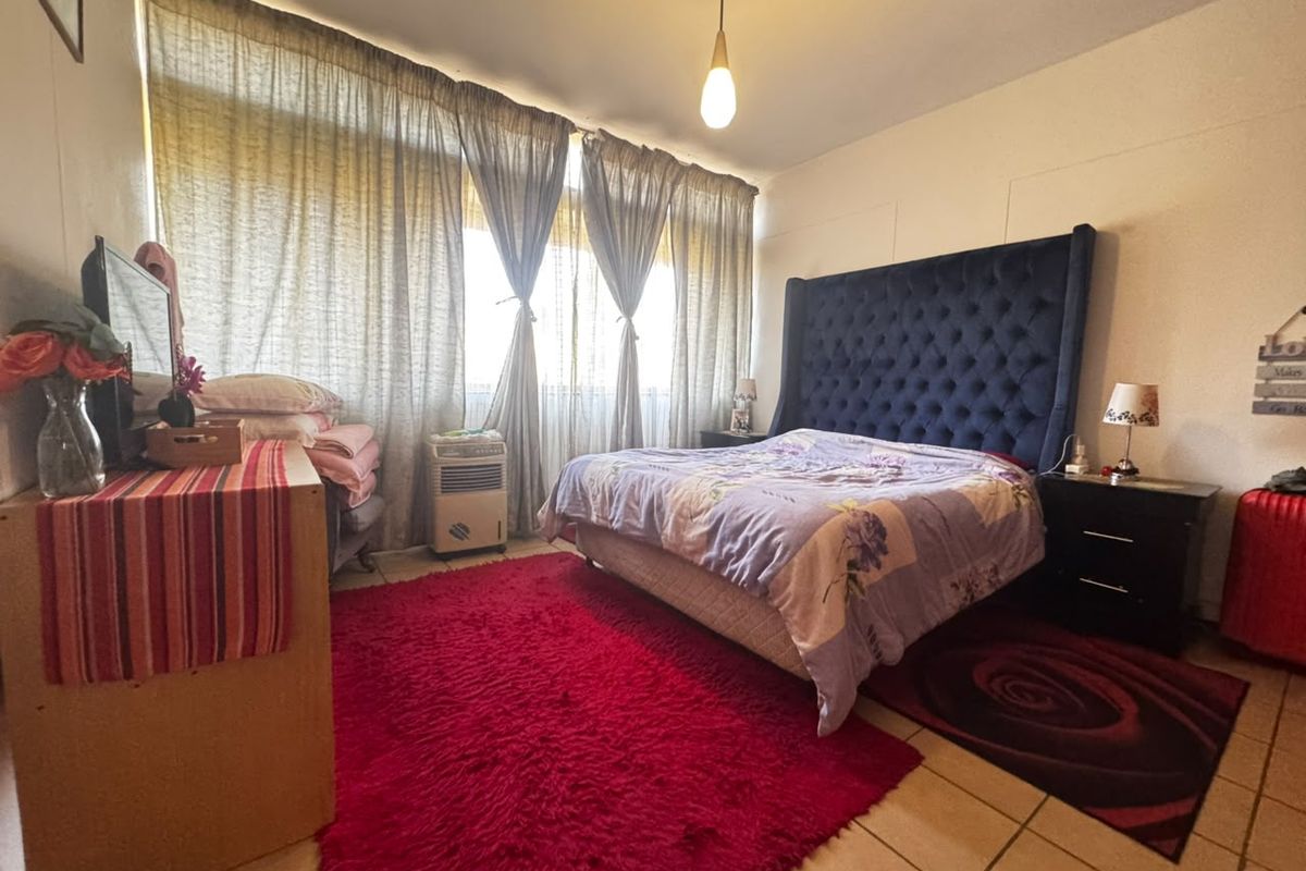 A spacious bedroom featuring tiled flooring, a large window with curtains, and a central pendant light fixture.