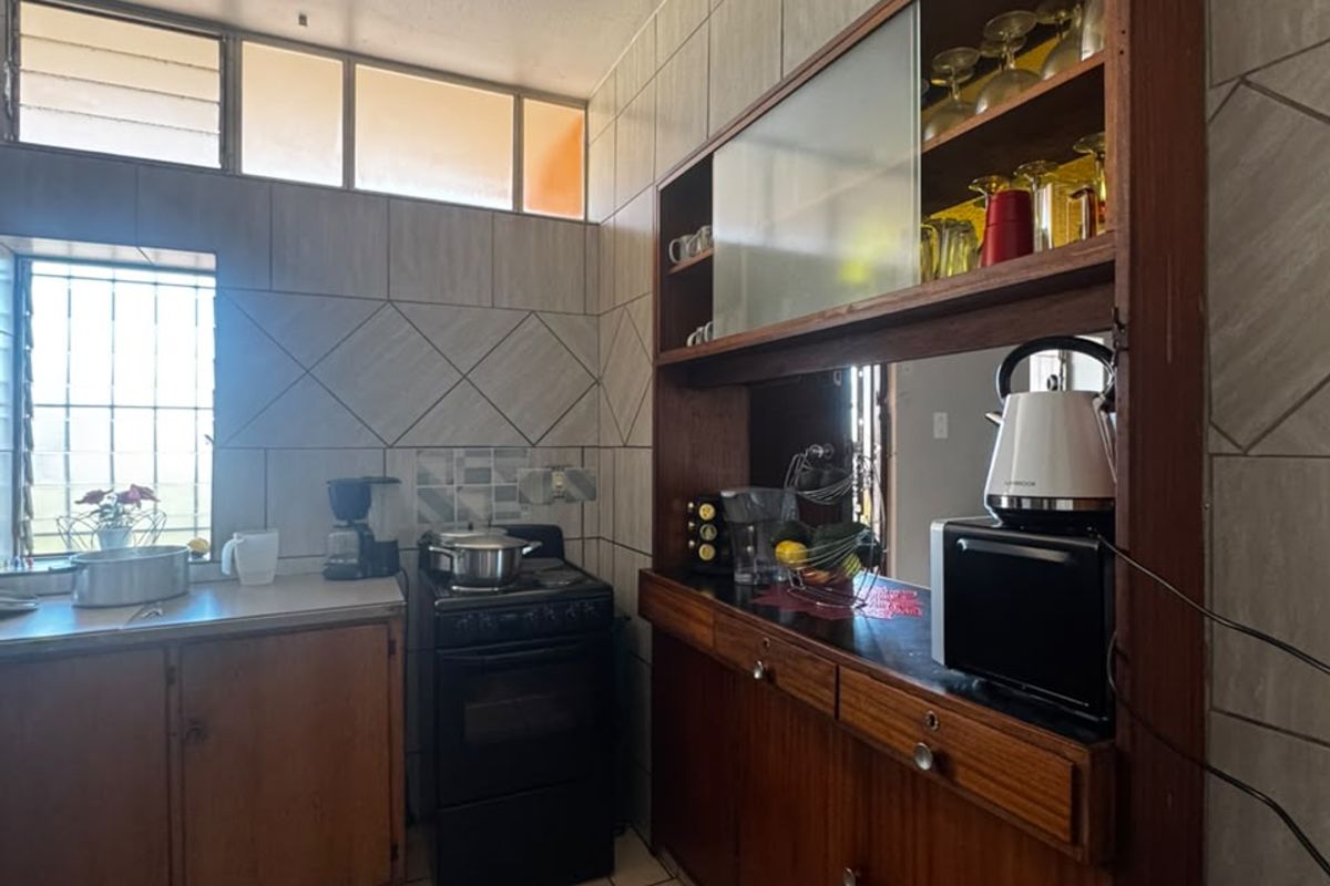 A functional kitchen featuring built-in wooden cabinetry, tiled walls, and tiled flooring, offering a classic layout with ample storage and natural light.