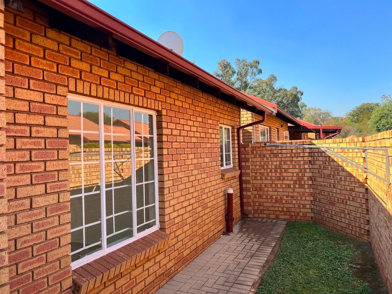 A well-maintained rear exterior view of the apartment featuring face brick walls, a paved walkway, and a private brick-walled garden area.