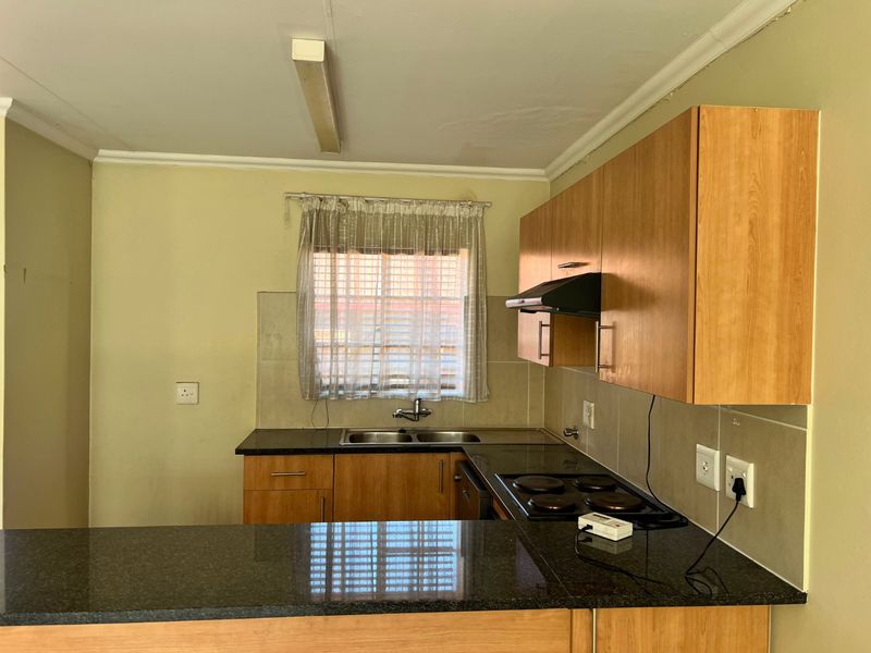 A functional kitchen featuring laminate cabinetry, granite countertops, a double bowl sink, and a built-in electric hob with an extractor fan.