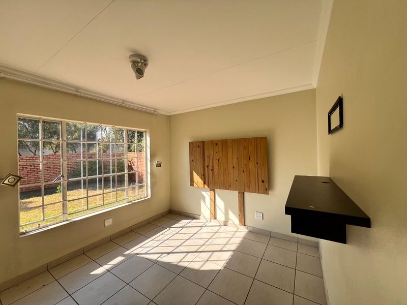 A bright, empty living room featuring tiled flooring, a large window with garden views, and wall-mounted shelving, offering a clean canvas for personalization.