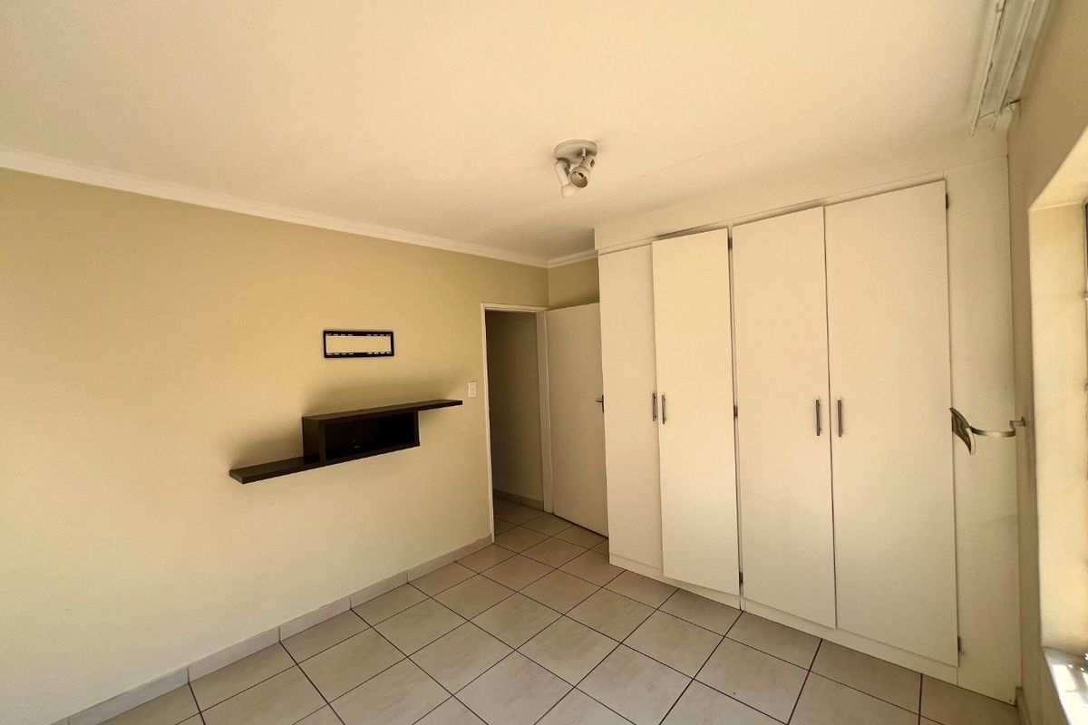 A clean, empty bedroom featuring neutral tiled flooring, built-in white cupboards, and a wall-mounted shelf, offering a blank canvas for personalization.