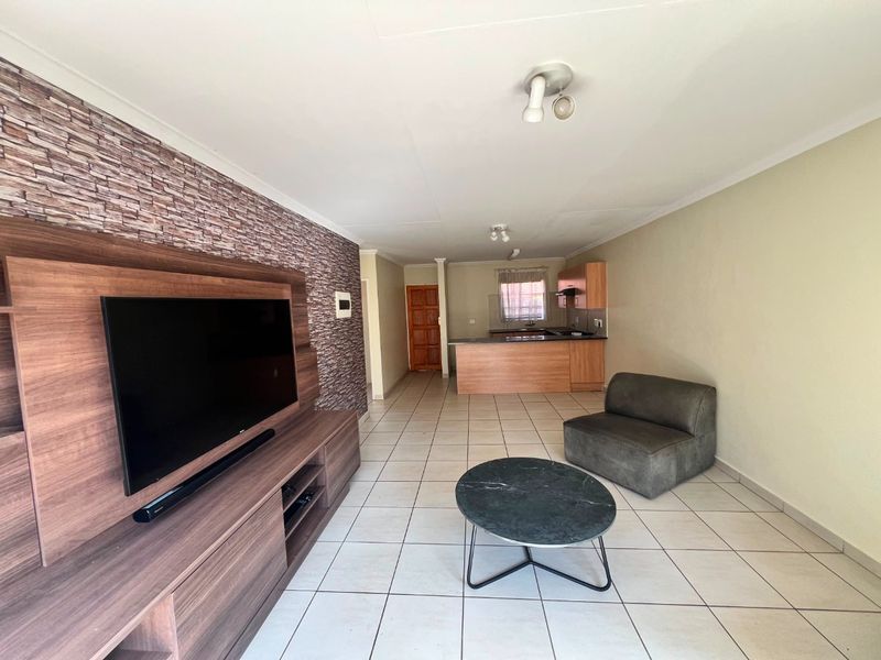 Open-plan living area featuring tiled floors, a stone-cladding feature wall, and an integrated kitchen with a breakfast bar.