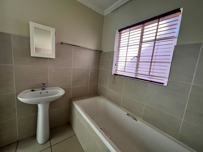 A functional bathroom featuring a pedestal basin, a bathtub, and neutral wall tiling with a window for natural light.