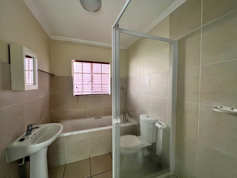 A functional bathroom featuring a pedestal basin, built-in bathtub, and a separate shower enclosure with tiled finishes throughout.