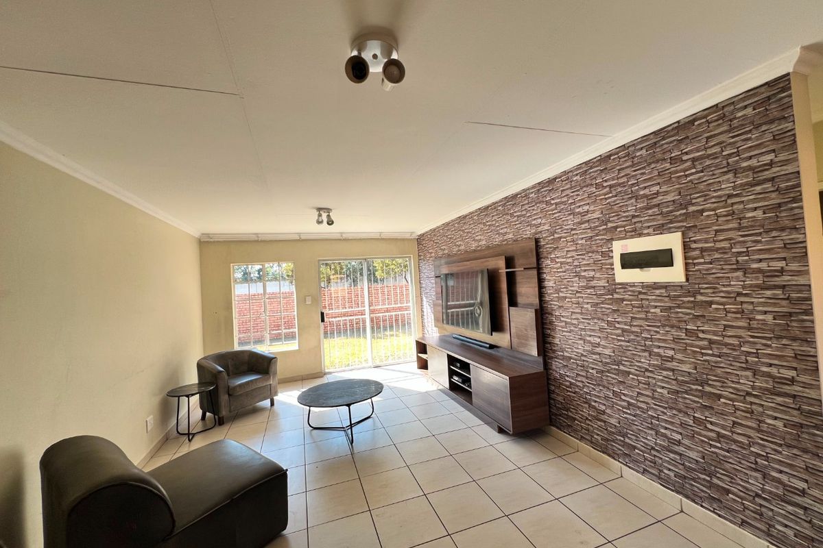 Spacious living room featuring tiled floors, a stone-cladding feature wall, and a sliding glass door providing access to the exterior.