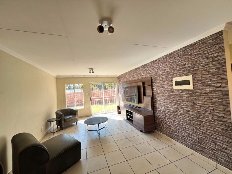 Spacious living room featuring tiled floors, a stone-cladding feature wall, and a sliding glass door providing access to the exterior.