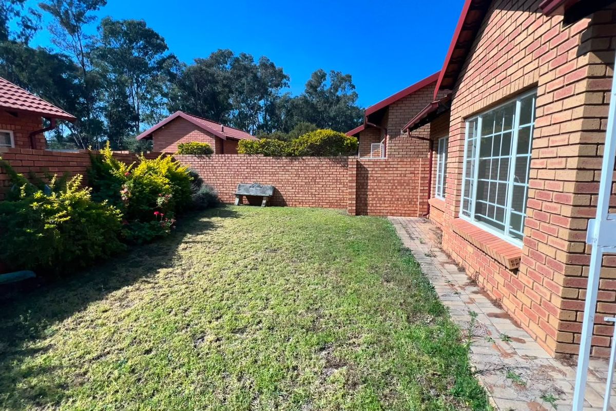 A private rear garden featuring a brick boundary wall, a small lawn area, and a paved walkway alongside the apartment building.