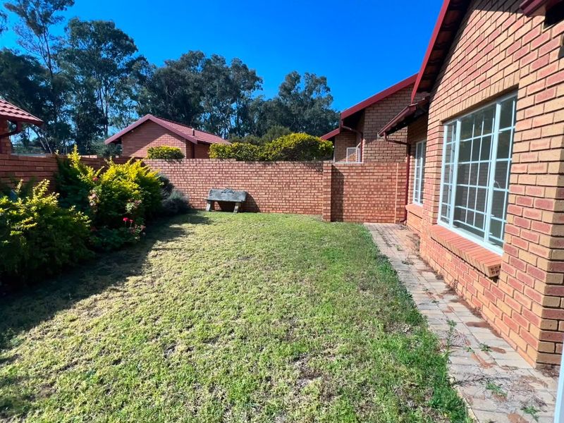 A private rear garden featuring a brick boundary wall, a small lawn area, and a paved walkway alongside the apartment building.