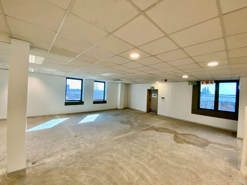 An empty, open-plan commercial office space featuring a suspended ceiling, recessed lighting, and large windows with views.