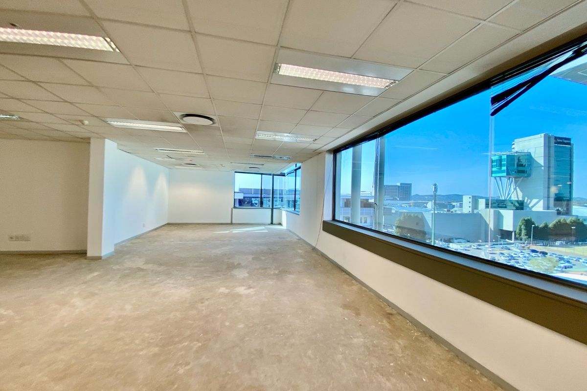 An open-plan commercial office space featuring a suspended ceiling, recessed lighting, and large windows with expansive city views, currently in a shell condition.