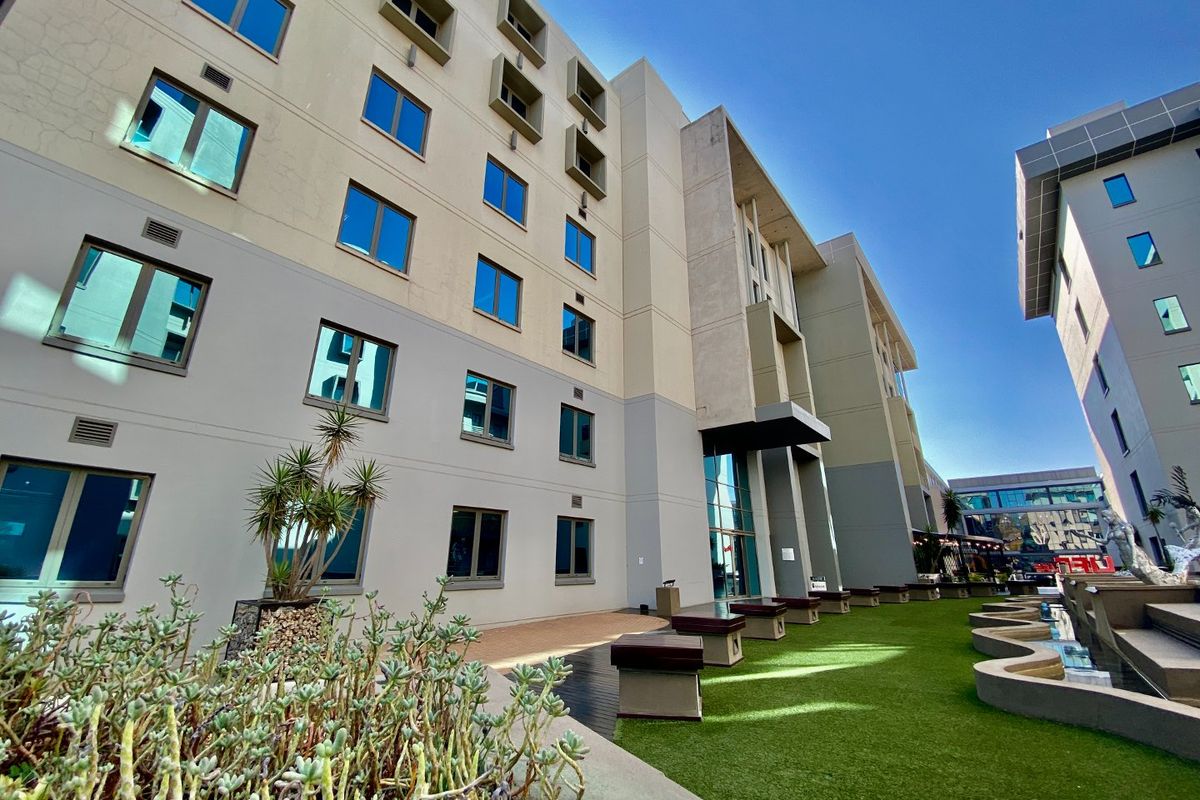 A modern commercial building exterior featuring a multi-story facade, landscaped artificial lawn area, and integrated water features.