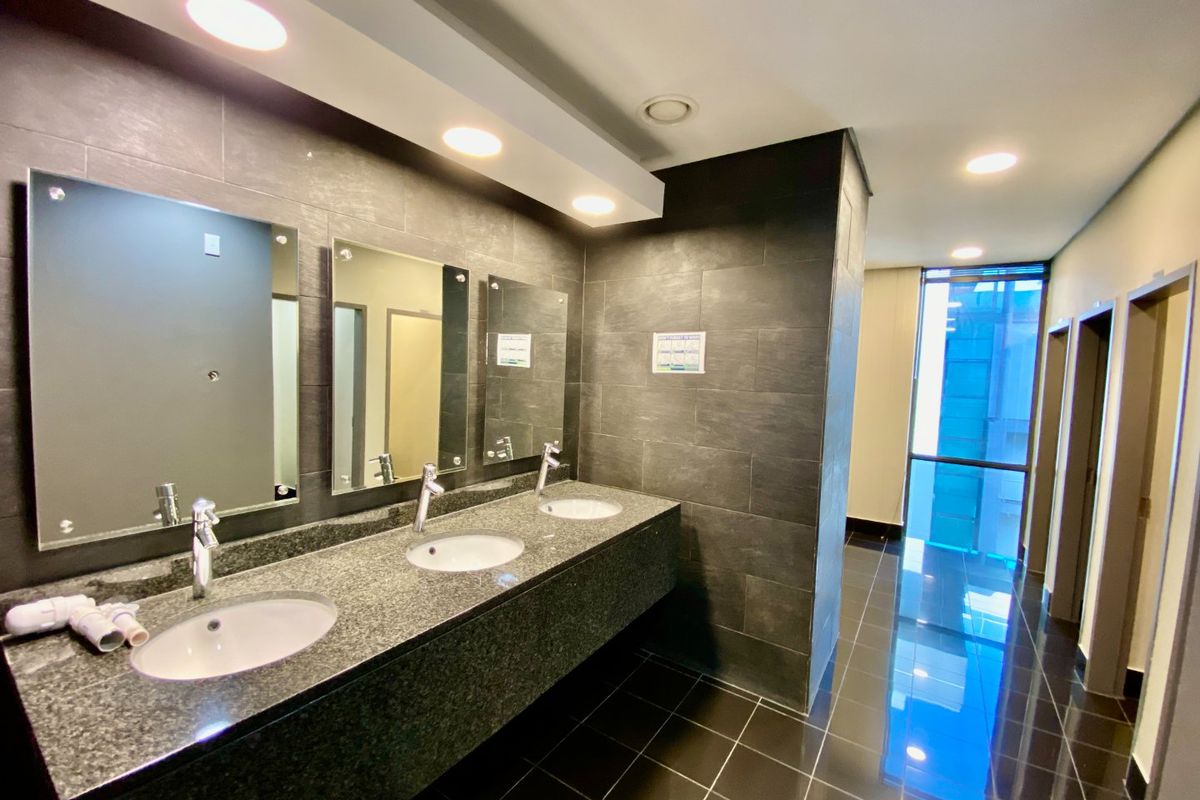 Modern commercial bathroom featuring a granite vanity with triple undermount sinks, dark ceramic tiling, and recessed lighting in a clean, well-maintained space.