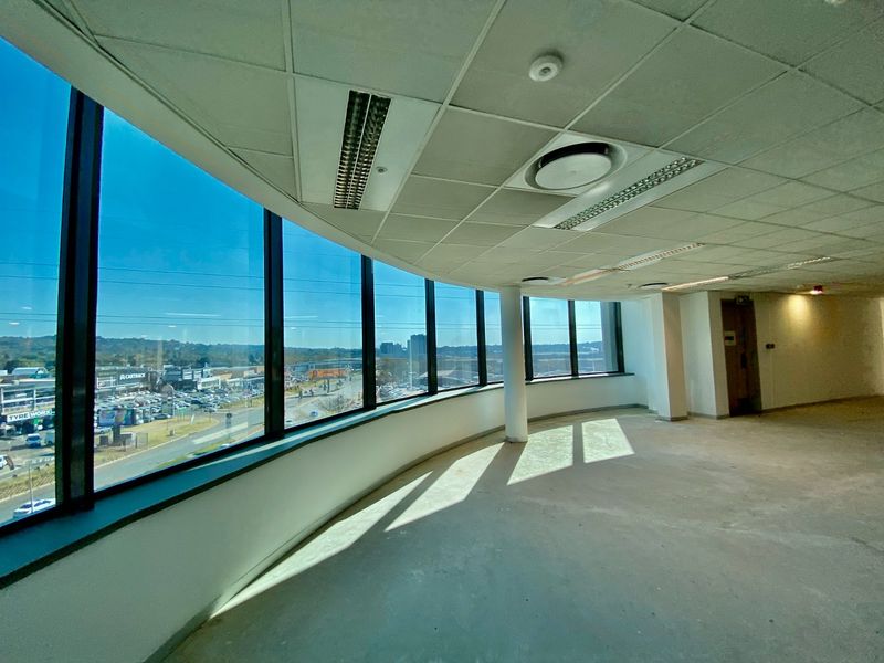 Spacious open-plan office area featuring floor-to-ceiling windows with expansive views, suspended ceilings, and recessed lighting in a commercial building.