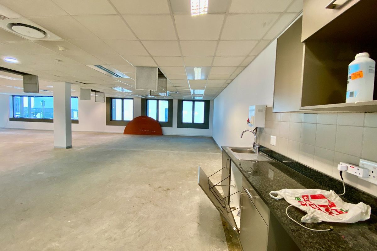 An open-plan commercial office space featuring a small kitchenette area with granite countertops, stainless steel sink, and built-in cabinetry.