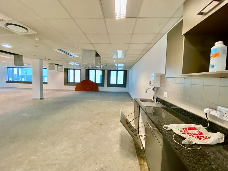 An open-plan commercial office space featuring a small kitchenette area with granite countertops, stainless steel sink, and built-in cabinetry.