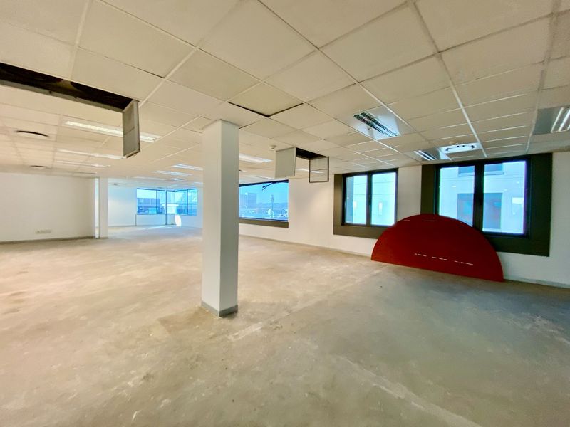 An open-plan commercial office space featuring a suspended ceiling, structural columns, and large windows, currently in a shell condition awaiting fit-out.