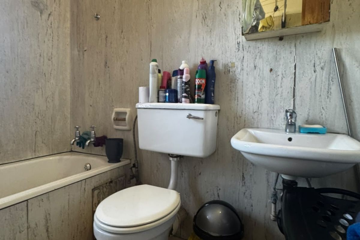 A dated bathroom featuring a bathtub, toilet, and wall-mounted basin with tiled wall finishes, requiring cosmetic updates and modernization.