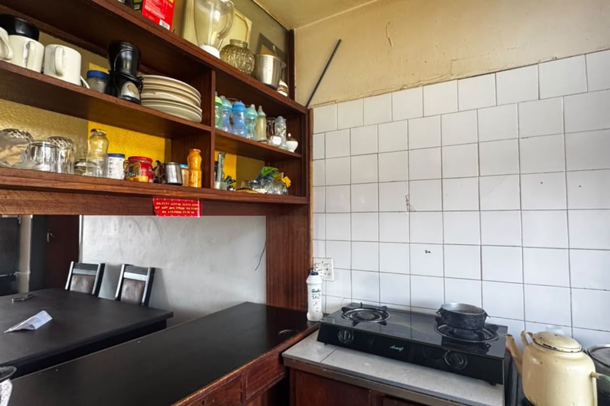 A compact kitchen featuring dark wood cabinetry, open shelving, a tiled backsplash, and a built-in gas hob and oven combination.