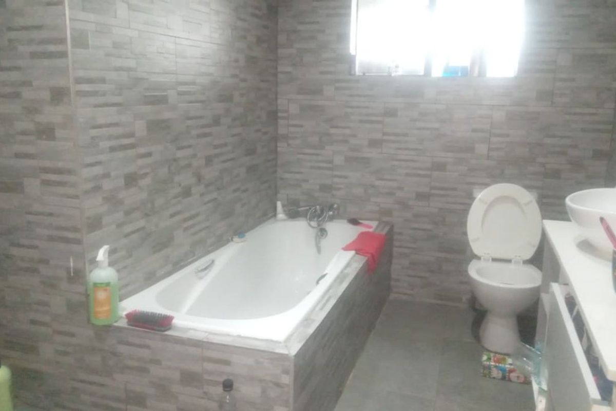 A functional bathroom featuring a built-in bathtub, toilet, and vanity basin with modern grey textured wall tiling.