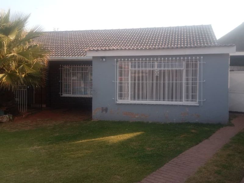 Front view of a single-story house featuring a tiled roof, security bars on windows, a front lawn, and a paved driveway with a gated entrance.