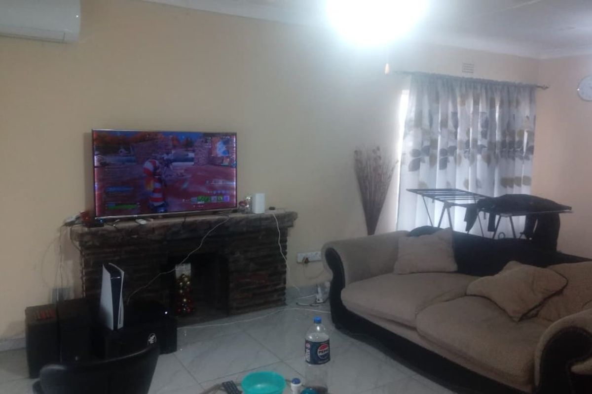 A living room featuring a stone fireplace, tiled flooring, and a wall-mounted air conditioning unit.