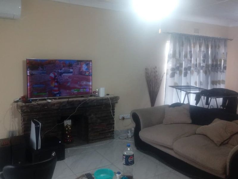 A living room featuring a stone fireplace, tiled flooring, and a wall-mounted air conditioning unit.