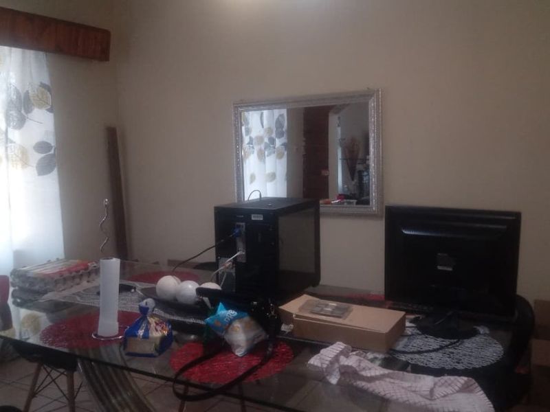 A dining room area featuring tiled flooring and a window with a decorative pelmet, currently utilized as a workspace.