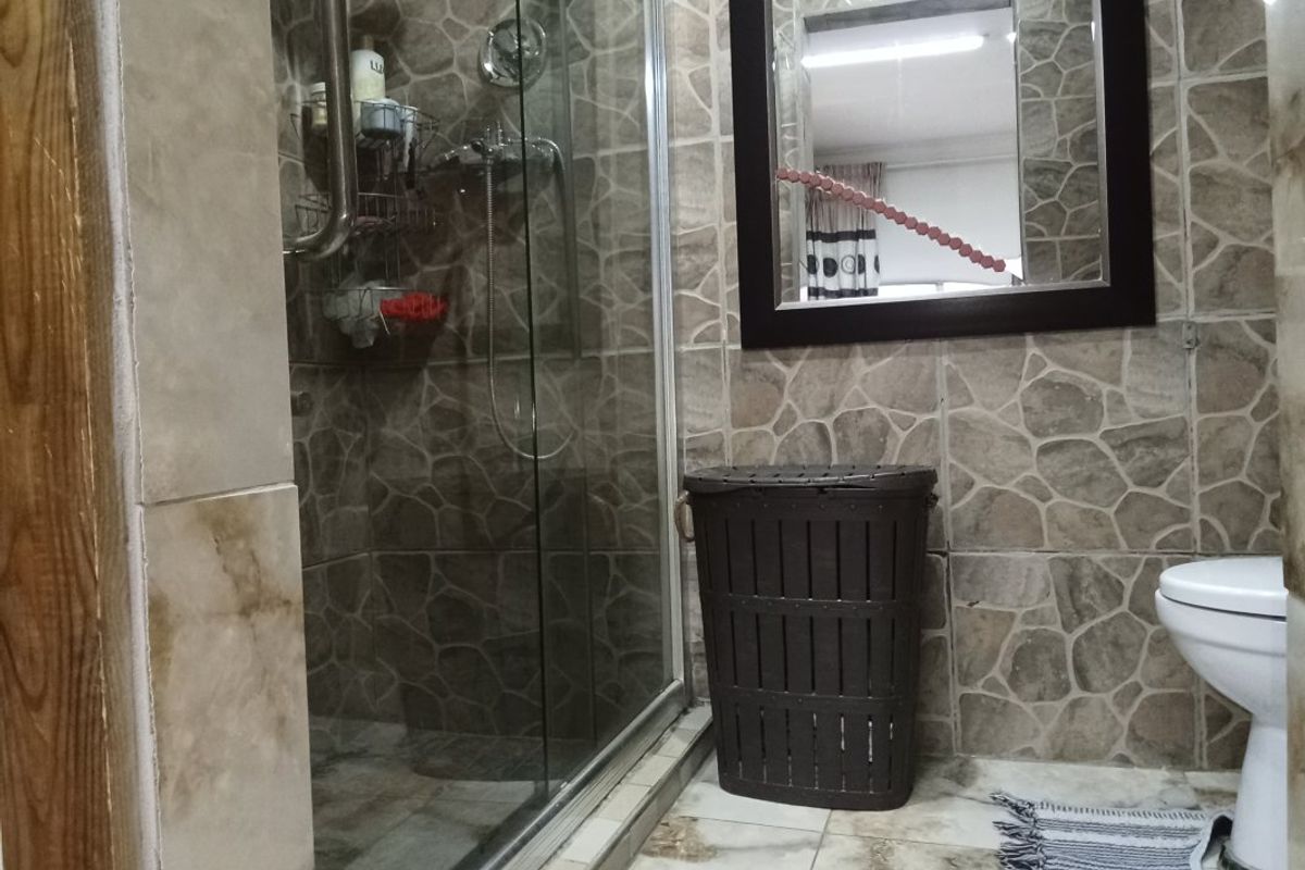 A functional bathroom featuring a glass-enclosed shower, wall-mounted mirror, and tiled finishes throughout.