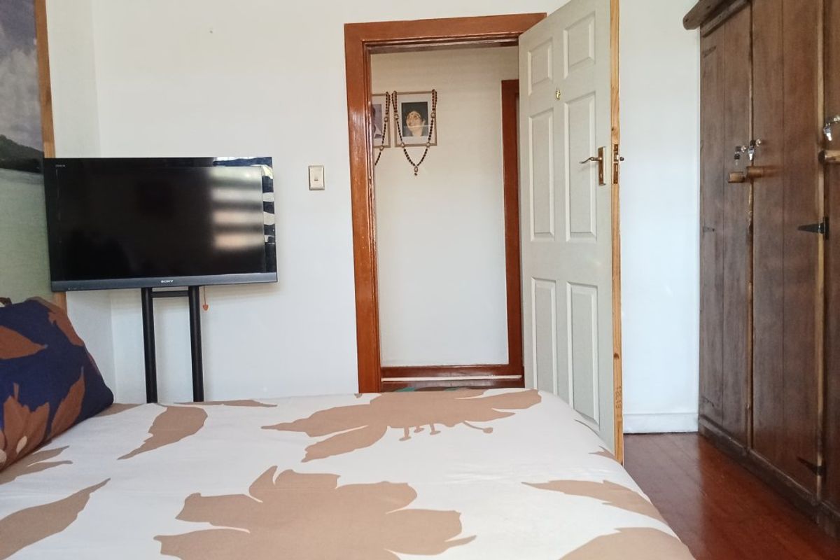 A bedroom featuring timber flooring, a built-in wardrobe, and a traditional timber door frame, offering a functional space with potential for cosmetic updates.