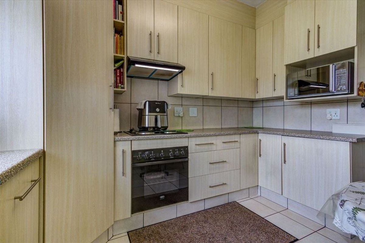 A functional kitchen featuring light wood-finish cabinetry, granite countertops, a built-in oven with hob, extractor fan, and integrated microwave with tiled backsplash.