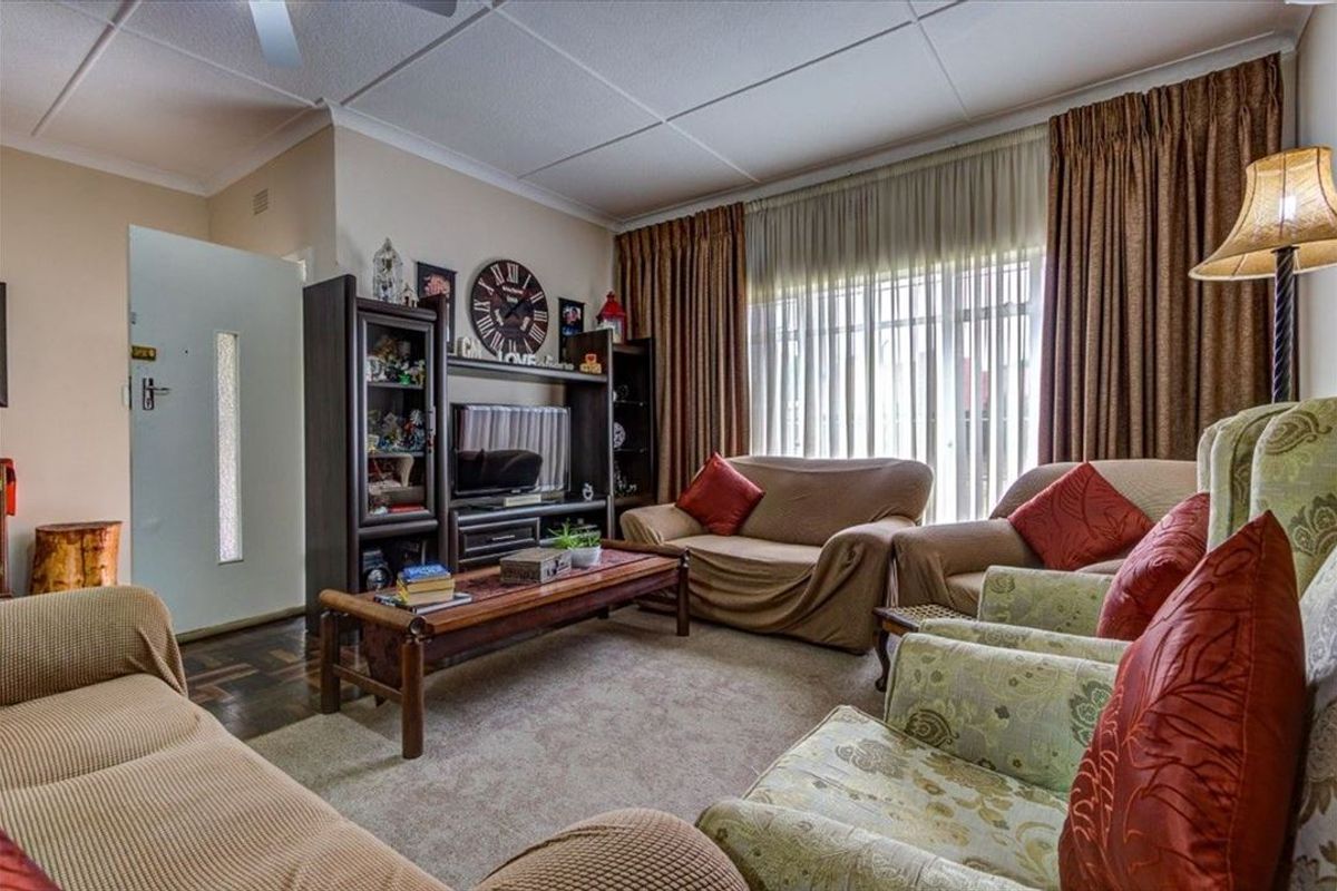A comfortable living room featuring parquet flooring, coved cornicing, and a ceiling fan, with large windows providing natural light.