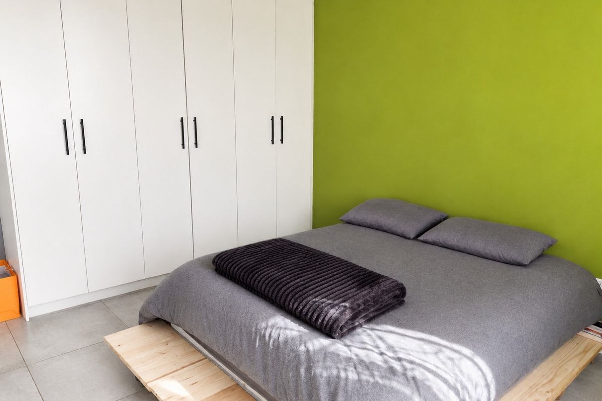 A bedroom featuring modern white built-in wardrobes, tiled flooring, and a vibrant green accent wall.