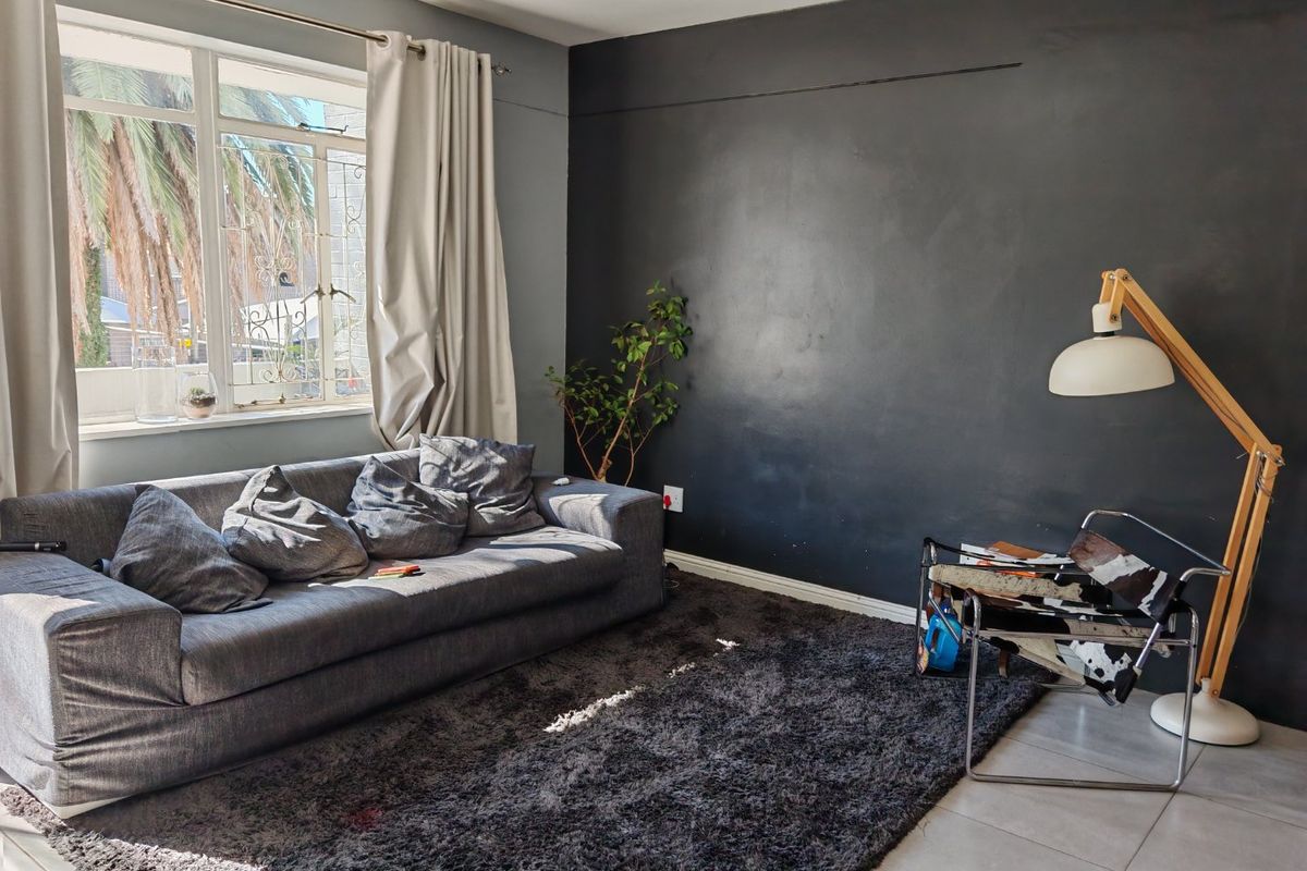 A living room featuring tiled flooring, a large window with security bars, and a dark accent wall with a visible surface crack.