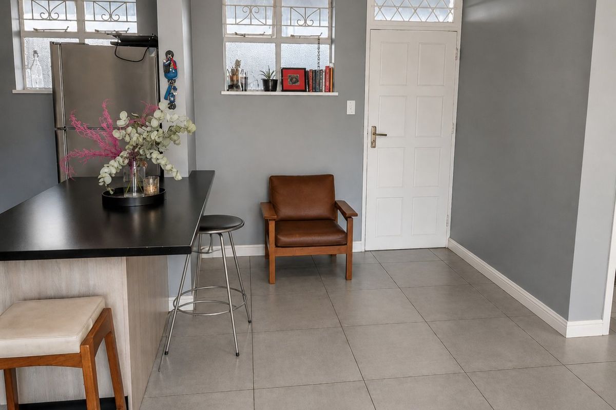 A modern kitchen area featuring a sleek black island, neutral grey wall tones, and large format floor tiles.