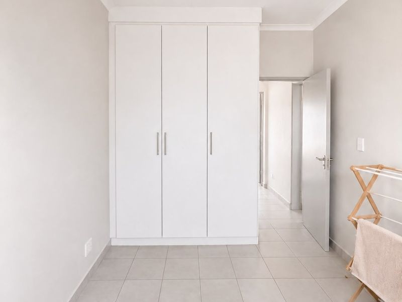 A clean, neutral bedroom featuring large built-in wardrobes, tiled flooring, and a simple ceiling light fixture, offering a bright and functional living space.