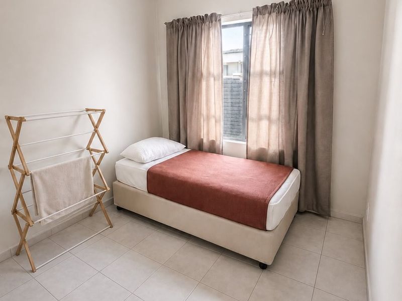 A compact bedroom featuring neutral tiled flooring, a single window with curtains, and a ceiling light fixture.
