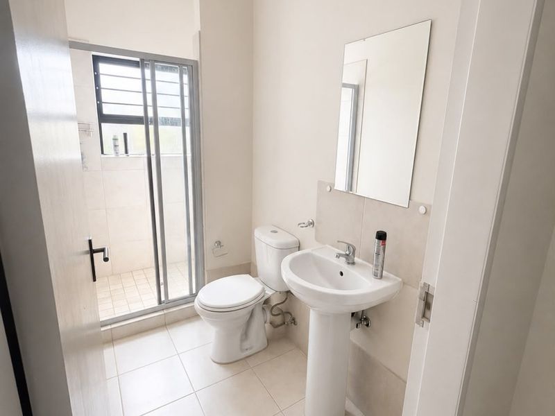 A clean, functional bathroom featuring a pedestal basin, toilet, and a separate shower enclosure with tiled flooring and neutral wall finishes.