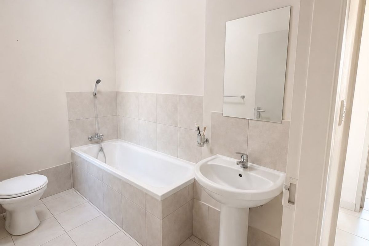 A clean and functional bathroom featuring a pedestal basin, a built-in bathtub with shower mixer, and neutral floor-to-wall tiling.