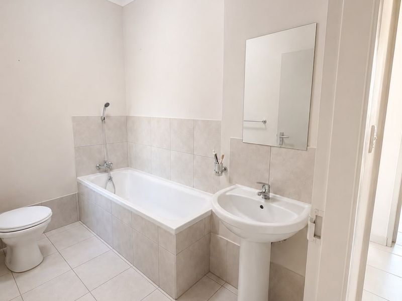 A clean and functional bathroom featuring a pedestal basin, a built-in bathtub with shower mixer, and neutral floor-to-wall tiling.