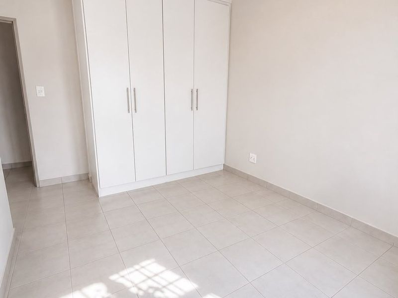 A bright, empty bedroom featuring neutral tiled flooring, clean white walls, and a spacious built-in wardrobe with modern handles.