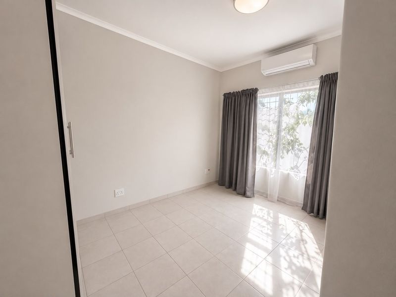 A bright, empty bedroom featuring neutral tiled flooring, a built-in wardrobe, and a wall-mounted split-system air conditioner.