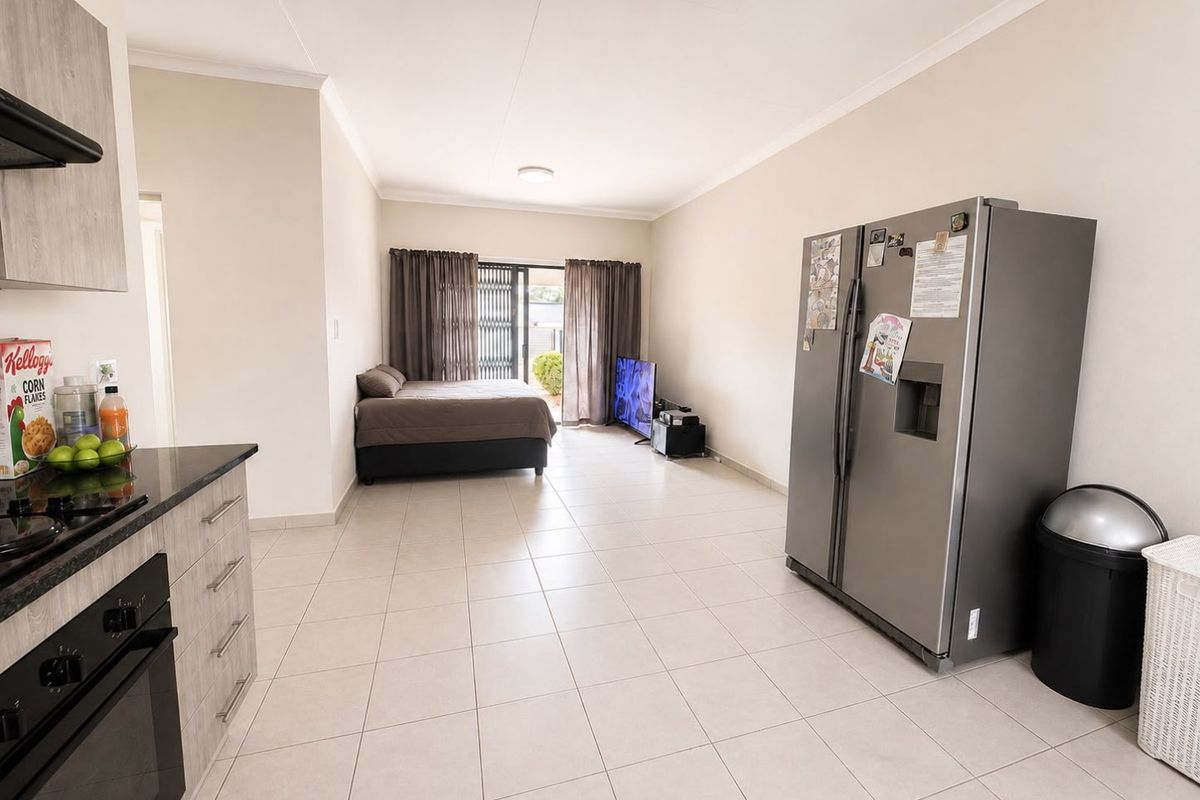 Open-plan living area featuring tiled flooring, a compact kitchen with built-in appliances, and sliding door access to the exterior.