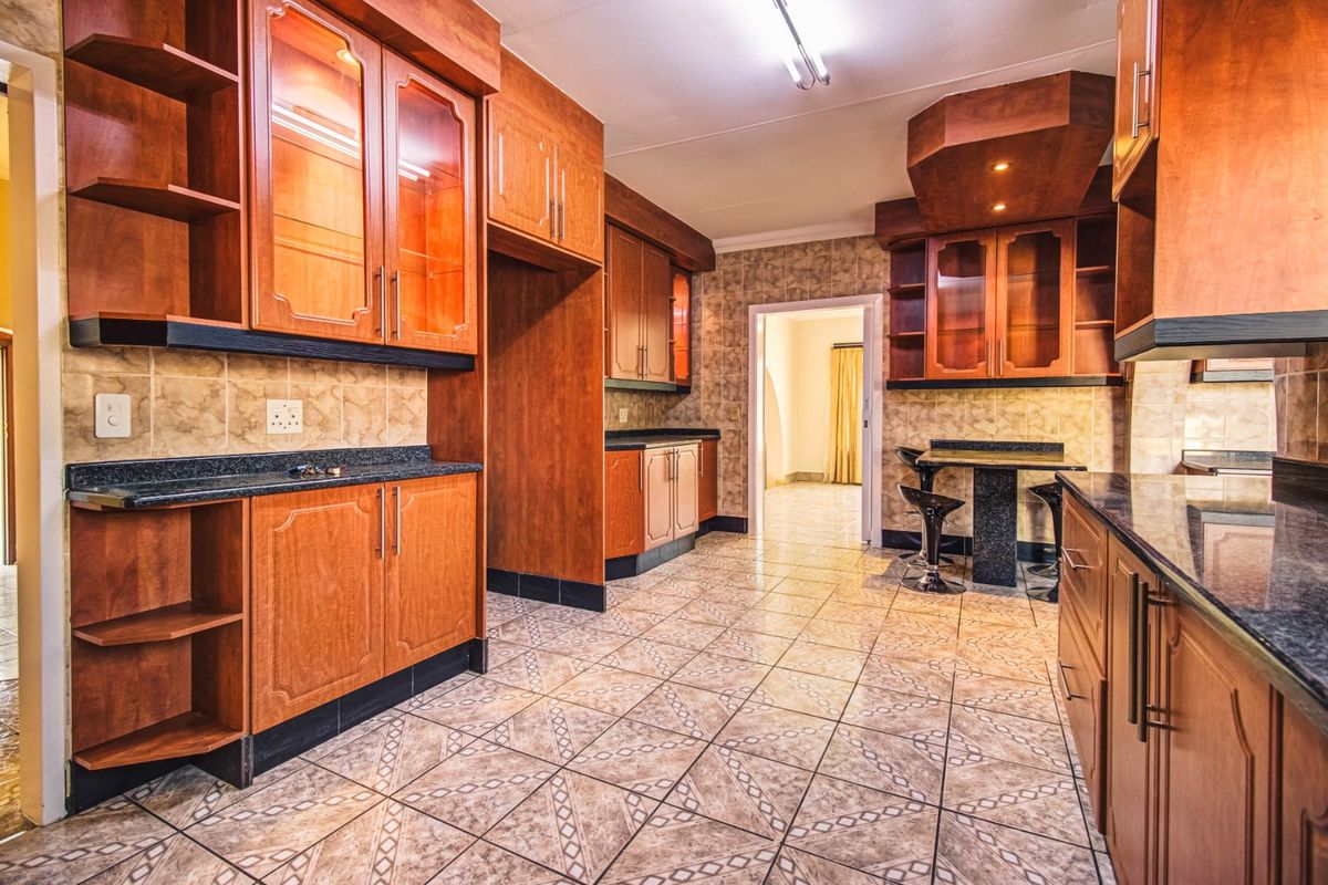 A spacious kitchen featuring extensive wooden cabinetry, granite countertops, tiled flooring, and a built-in breakfast bar area.