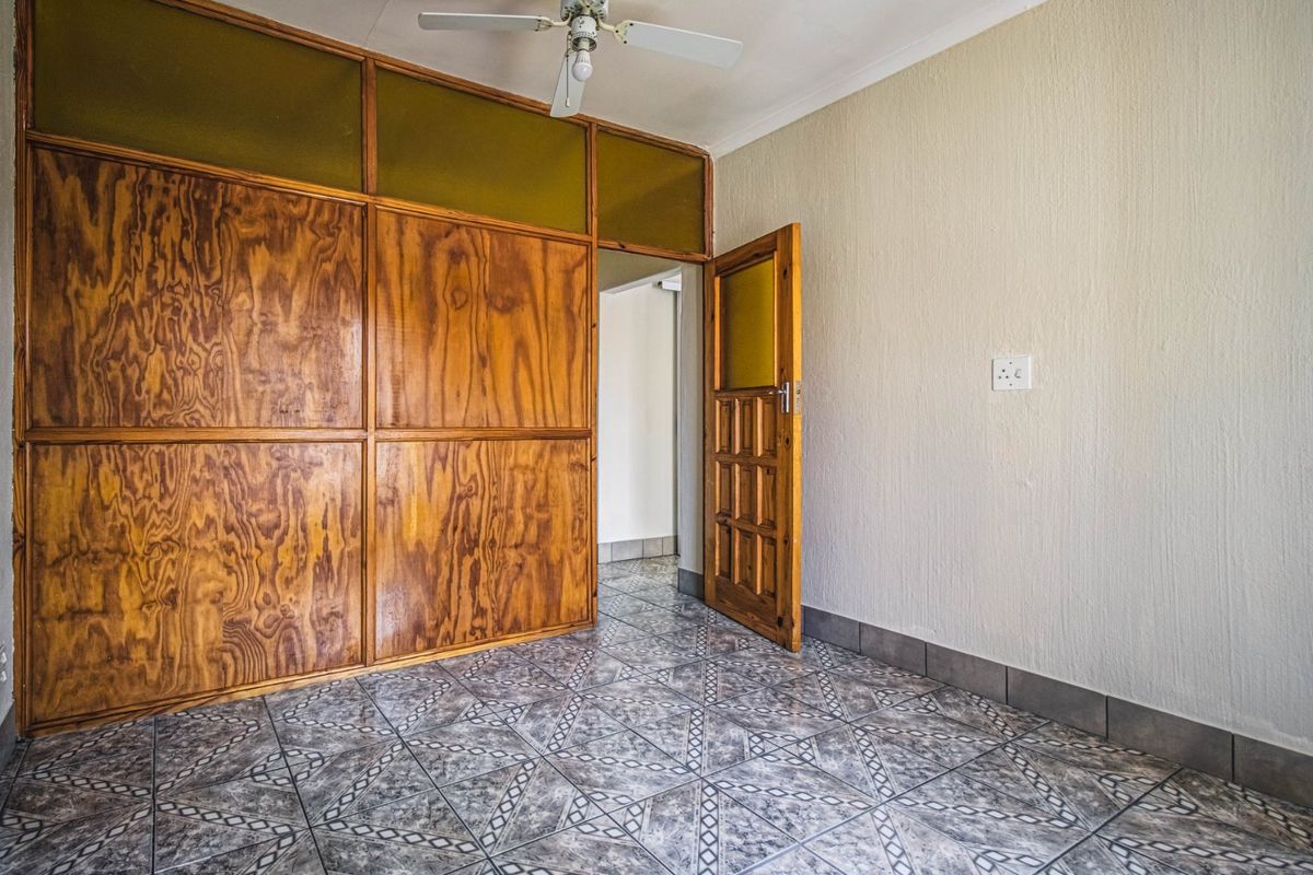 An empty bedroom featuring tiled flooring, a ceiling fan, and extensive built-in wooden cabinetry with integrated storage.