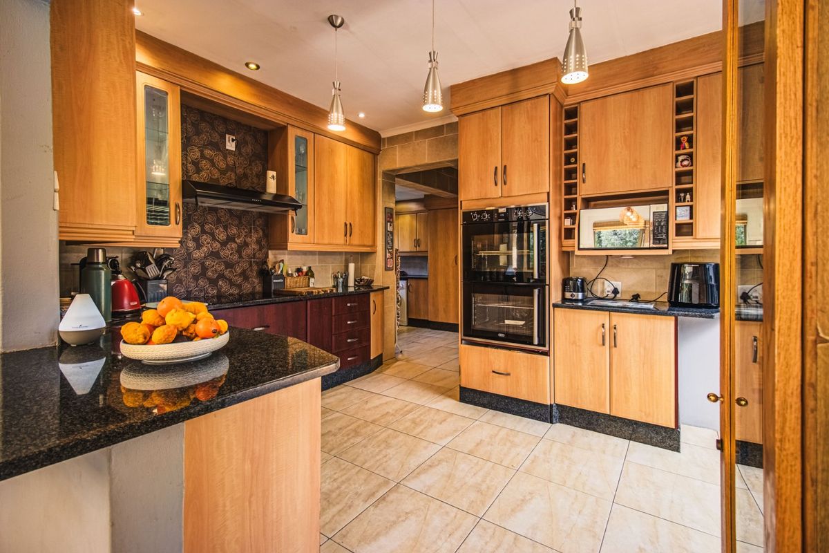 A functional kitchen featuring light wood cabinetry, granite countertops, tiled flooring, and integrated appliances including a double wall oven and extractor fan.