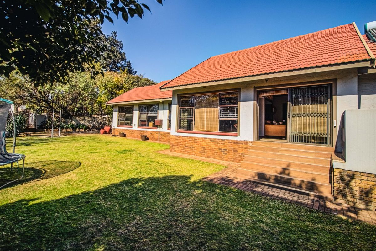 Rear view of the house featuring a tiled roof, brick exterior, and a paved patio area leading onto a well-maintained garden.
